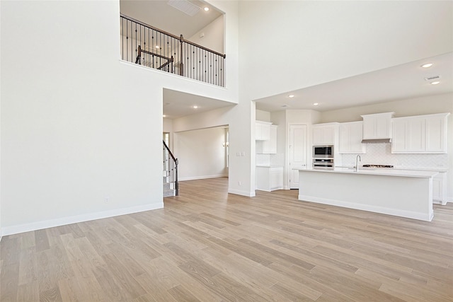 unfurnished living room featuring sink, light wood-type flooring, and a towering ceiling