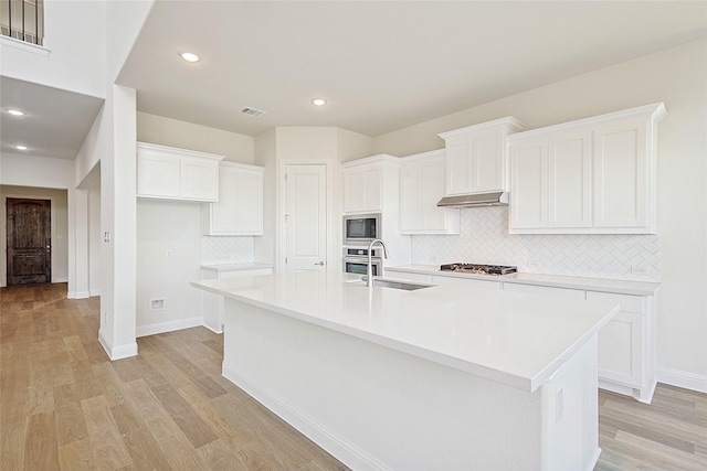 kitchen with an island with sink, built in microwave, white cabinets, and sink