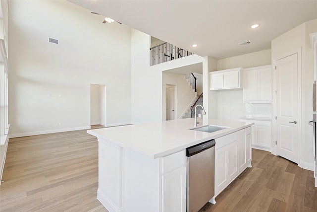 kitchen featuring dishwasher, light hardwood / wood-style flooring, a kitchen island with sink, white cabinetry, and sink