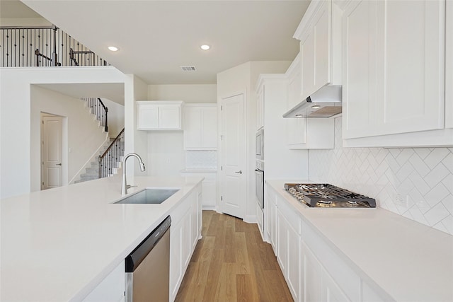 kitchen featuring light hardwood / wood-style flooring, tasteful backsplash, white cabinetry, appliances with stainless steel finishes, and sink