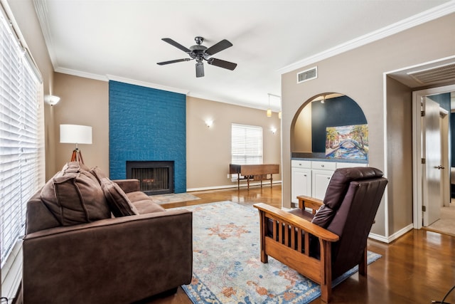 living room with a large fireplace, ornamental molding, dark hardwood / wood-style floors, and ceiling fan