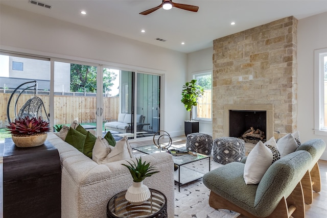 living room with light hardwood / wood-style floors, ceiling fan, and a stone fireplace