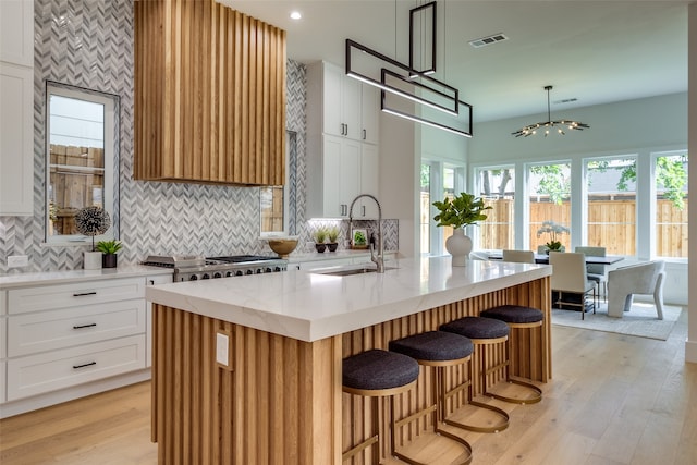 kitchen featuring light stone countertops, a center island with sink, light hardwood / wood-style floors, sink, and white cabinetry