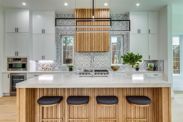 kitchen featuring wine cooler, oven, light stone countertops, pendant lighting, and a kitchen island with sink