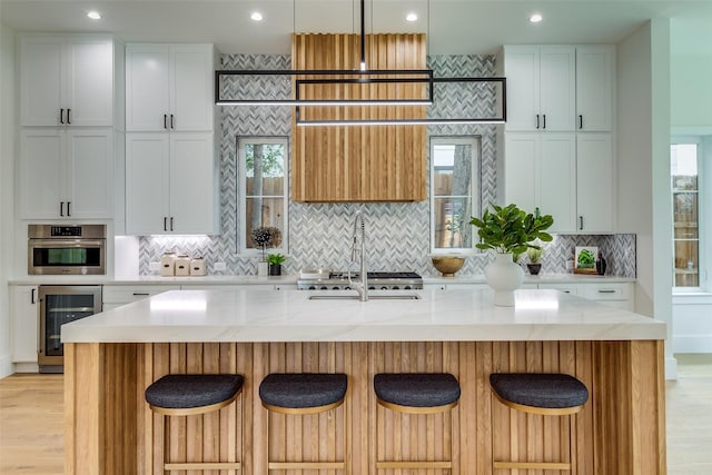 kitchen with stainless steel oven, wine cooler, light wood-style floors, and a center island with sink