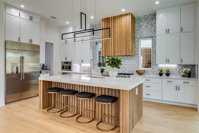 kitchen featuring light hardwood / wood-style floors, appliances with stainless steel finishes, a kitchen bar, and a center island with sink