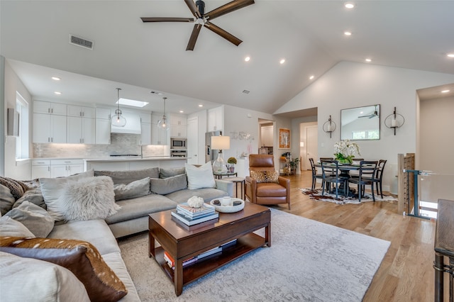 living room with light hardwood / wood-style floors, ceiling fan, and high vaulted ceiling