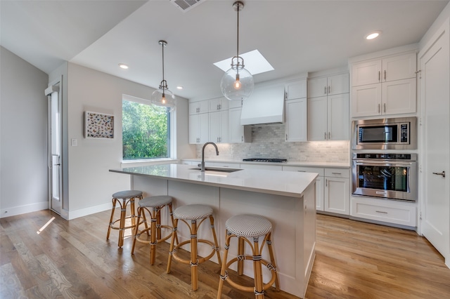 kitchen with white cabinetry, appliances with stainless steel finishes, a kitchen island with sink, and custom exhaust hood