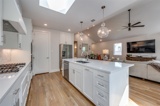 kitchen with custom range hood, white cabinets, vaulted ceiling with skylight, a kitchen island with sink, and sink