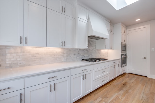 kitchen featuring white cabinets, a skylight, backsplash, appliances with stainless steel finishes, and light hardwood / wood-style floors