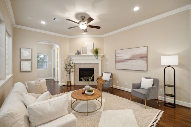 living room with ceiling fan, a tiled fireplace, dark hardwood / wood-style flooring, and ornamental molding