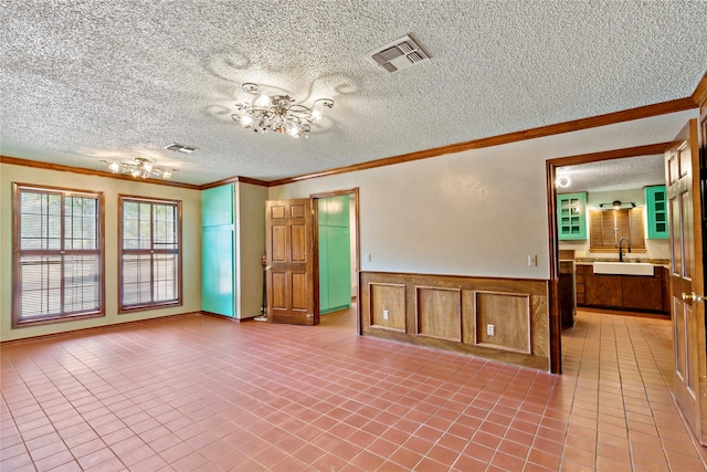 tiled empty room with a textured ceiling, crown molding, sink, and a notable chandelier