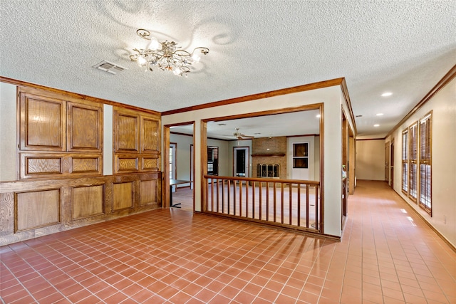 interior space with ceiling fan with notable chandelier, a brick fireplace, crown molding, and a textured ceiling