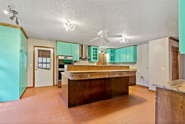 kitchen featuring a textured ceiling, light tile patterned floors, ceiling fan, double oven, and wall chimney range hood