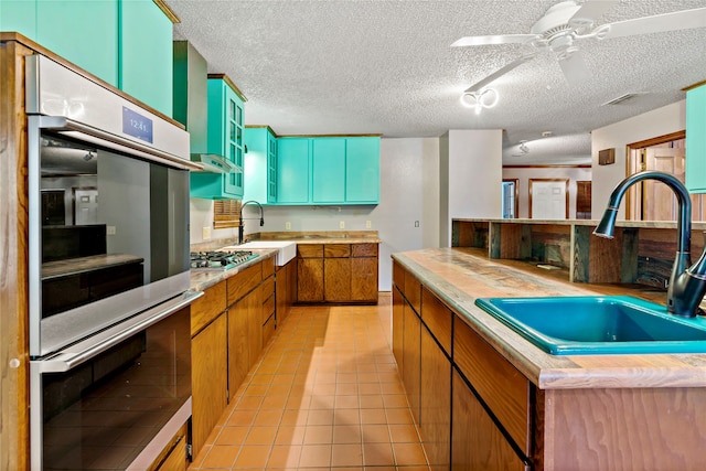 kitchen featuring a textured ceiling, stainless steel gas stovetop, wood counters, sink, and ceiling fan