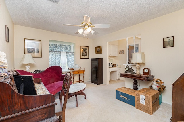 living room featuring ceiling fan, light colored carpet, and a textured ceiling