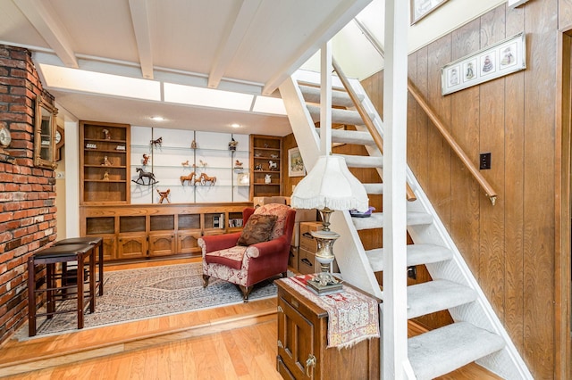 staircase featuring wooden walls, beamed ceiling, and wood-type flooring