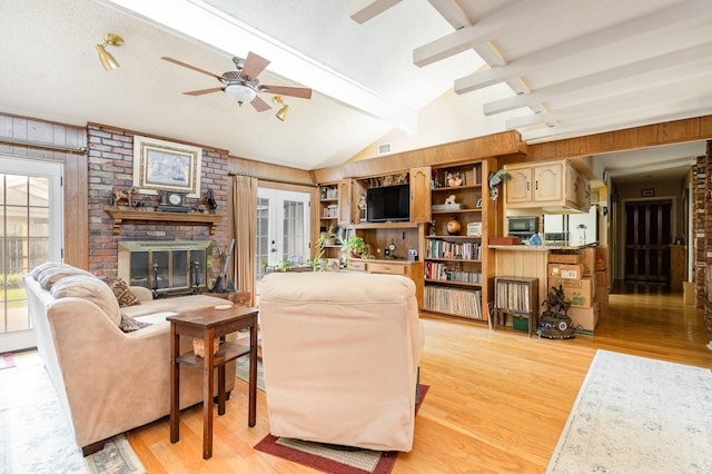 living room with ceiling fan, french doors, a brick fireplace, vaulted ceiling with beams, and light hardwood / wood-style floors