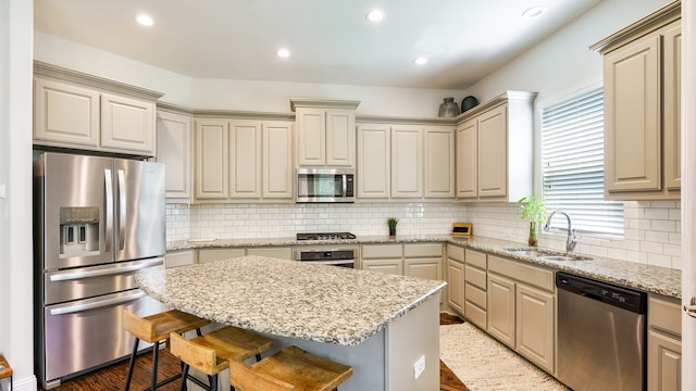 kitchen featuring wood-type flooring, appliances with stainless steel finishes, a kitchen bar, a center island, and sink