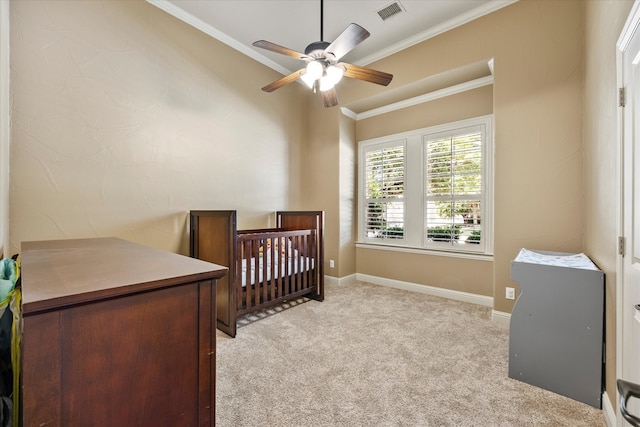 bedroom featuring a crib, light colored carpet, ceiling fan, and crown molding