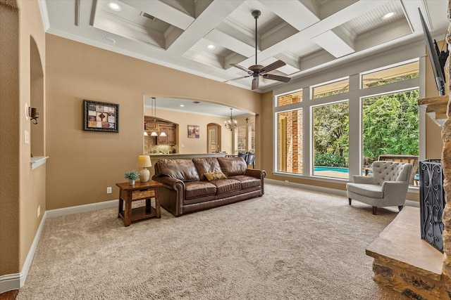 carpeted living room with ornamental molding, coffered ceiling, ceiling fan with notable chandelier, beamed ceiling, and a stone fireplace