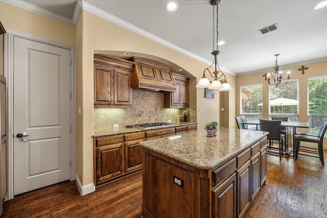 kitchen featuring pendant lighting, stainless steel gas stovetop, dark wood-type flooring, a notable chandelier, and a kitchen island