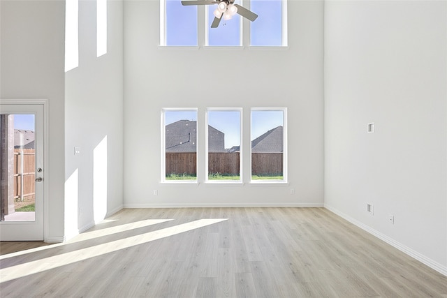 unfurnished living room featuring a high ceiling, light wood-type flooring, and ceiling fan