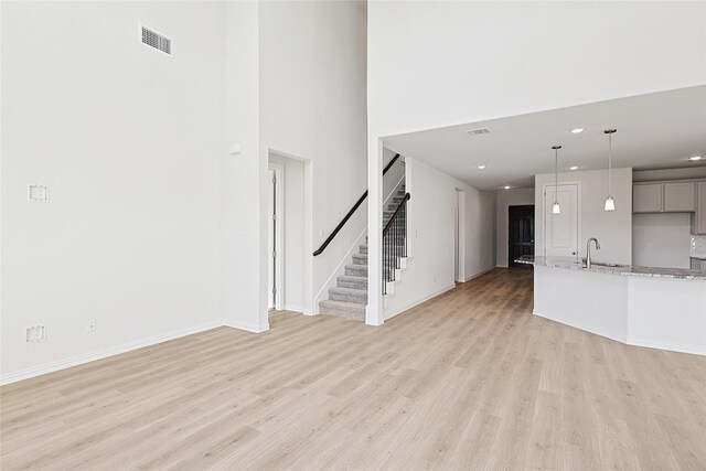 unfurnished living room with light hardwood / wood-style floors, ceiling fan with notable chandelier, and a towering ceiling