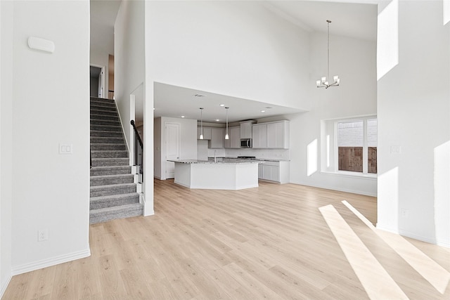 unfurnished living room with baseboards, stairway, an inviting chandelier, light wood-style floors, and a sink