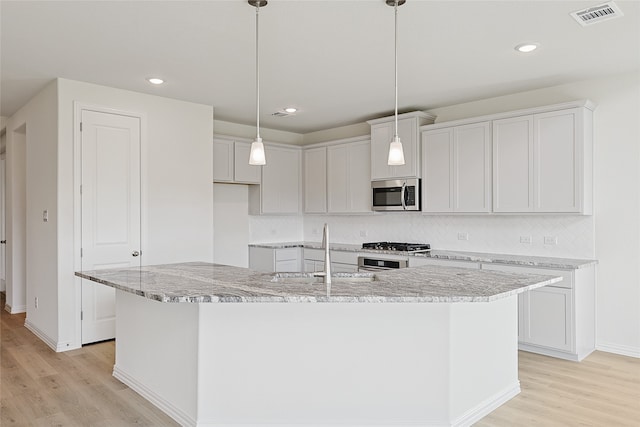 kitchen featuring stainless steel appliances, a center island with sink, and light wood-type flooring