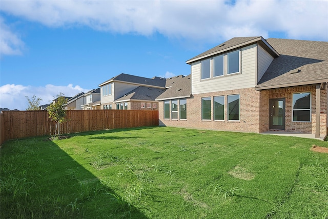 rear view of property featuring roof with shingles, brick siding, a lawn, a residential view, and a fenced backyard