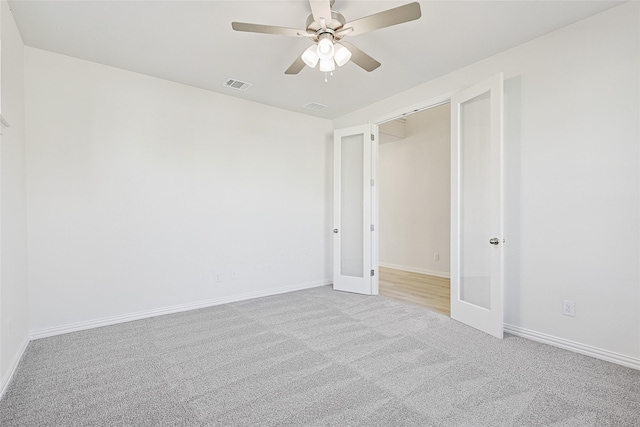 empty room featuring light carpet, ceiling fan, visible vents, and baseboards