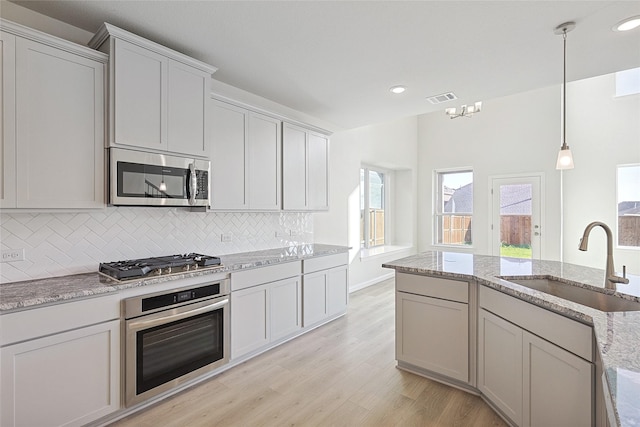 kitchen featuring visible vents, appliances with stainless steel finishes, light stone counters, decorative light fixtures, and a sink