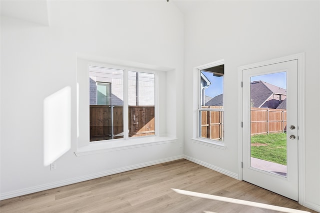 interior space with a high ceiling, light wood-type flooring, and baseboards