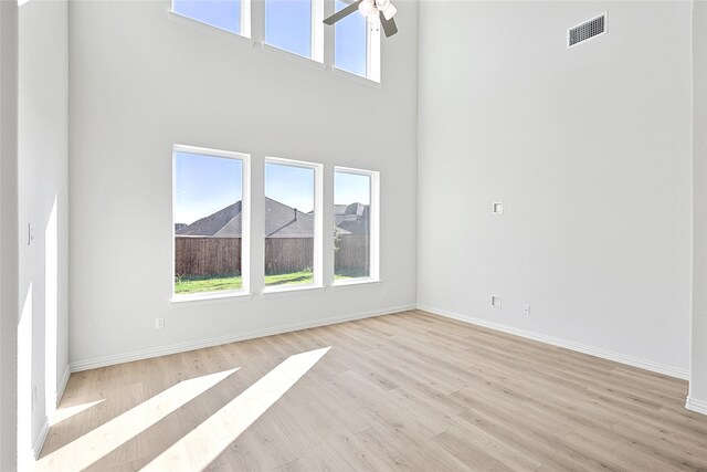 unfurnished living room featuring ceiling fan, a towering ceiling, visible vents, baseboards, and light wood finished floors