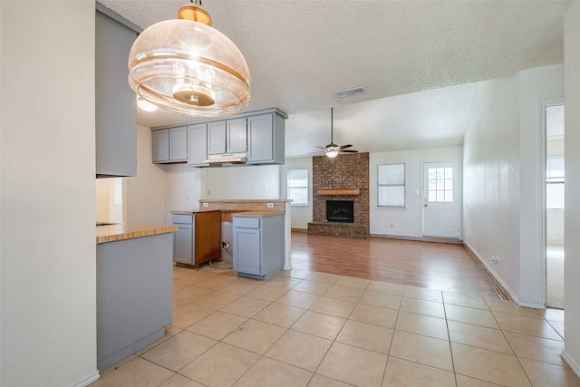 kitchen featuring hanging light fixtures, light tile patterned floors, a fireplace, ceiling fan, and a textured ceiling