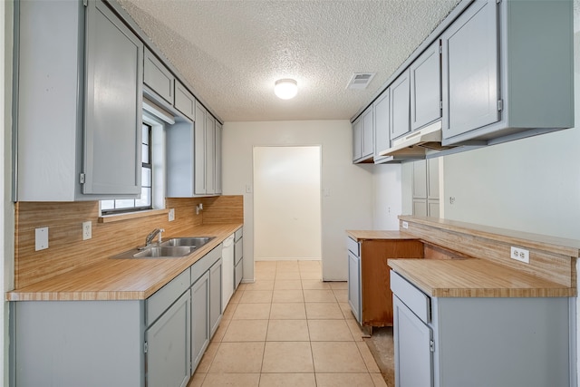 kitchen with gray cabinetry, light tile patterned floors, backsplash, sink, and a textured ceiling