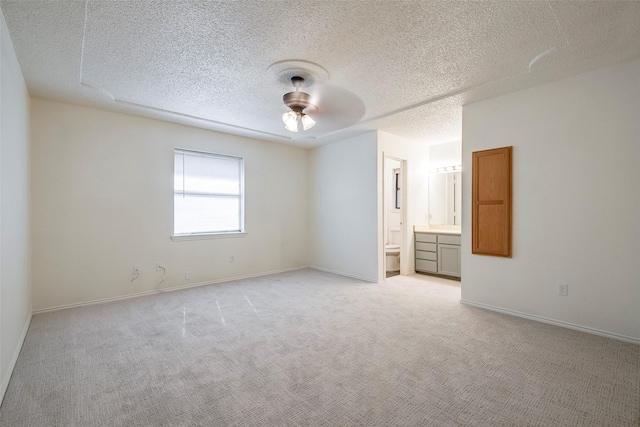 unfurnished bedroom featuring light carpet, baseboards, a ceiling fan, ensuite bath, and a textured ceiling