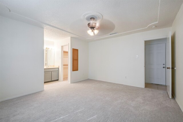 unfurnished bedroom featuring a textured ceiling, connected bathroom, ceiling fan, a closet, and light colored carpet