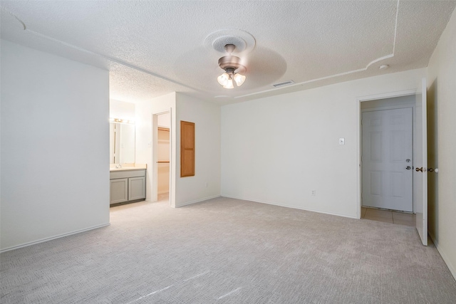 unfurnished bedroom featuring visible vents, light colored carpet, ceiling fan, ensuite bathroom, and a textured ceiling