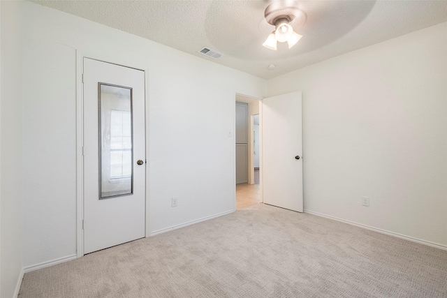 unfurnished room with light colored carpet, visible vents, ceiling fan, a textured ceiling, and baseboards