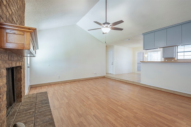 unfurnished living room with high vaulted ceiling, a textured ceiling, light hardwood / wood-style flooring, a brick fireplace, and ceiling fan