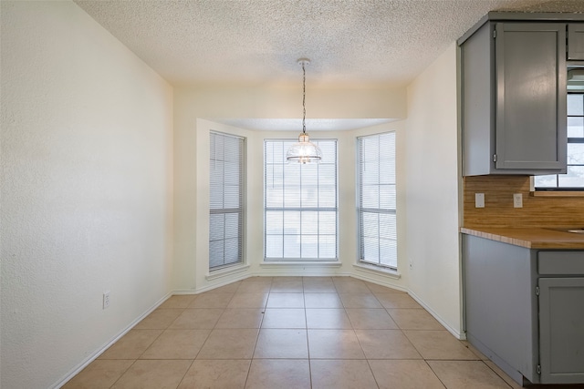 unfurnished dining area with light tile patterned floors, plenty of natural light, a chandelier, and a textured ceiling