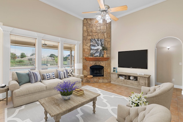 tiled living room with a stone fireplace, ornamental molding, and ceiling fan