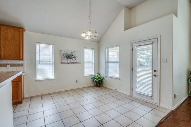 unfurnished dining area featuring light tile patterned floors, a notable chandelier, high vaulted ceiling, and baseboards