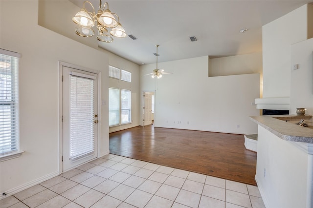 unfurnished dining area featuring light tile patterned flooring, ceiling fan with notable chandelier, a high ceiling, and baseboards