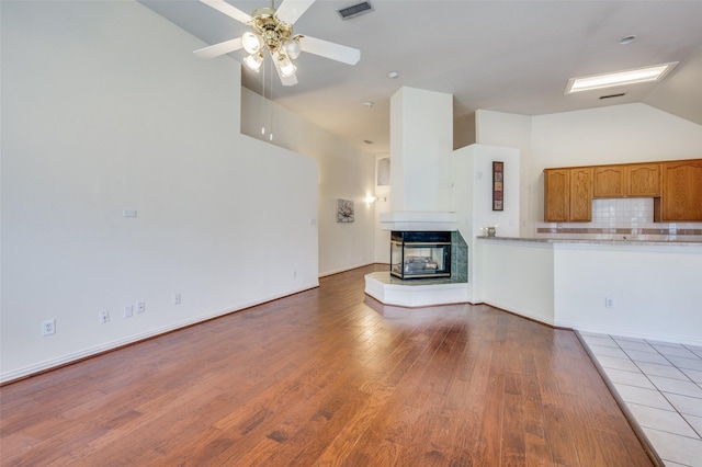 unfurnished living room featuring visible vents, ceiling fan, a multi sided fireplace, lofted ceiling, and wood finished floors