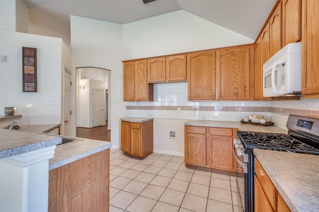 kitchen with white microwave, backsplash, gas range, light tile patterned floors, and arched walkways