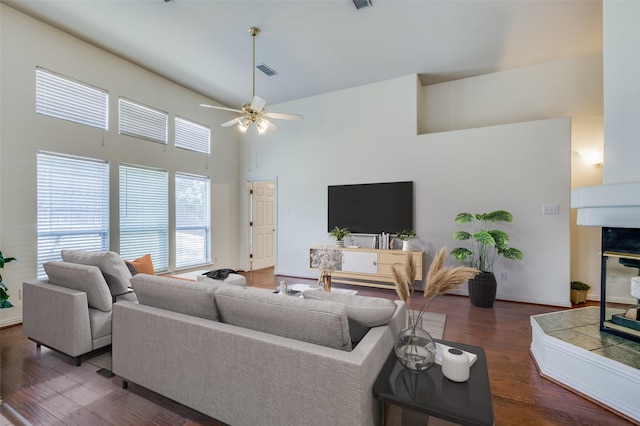 living area with a ceiling fan, wood finished floors, visible vents, baseboards, and a towering ceiling