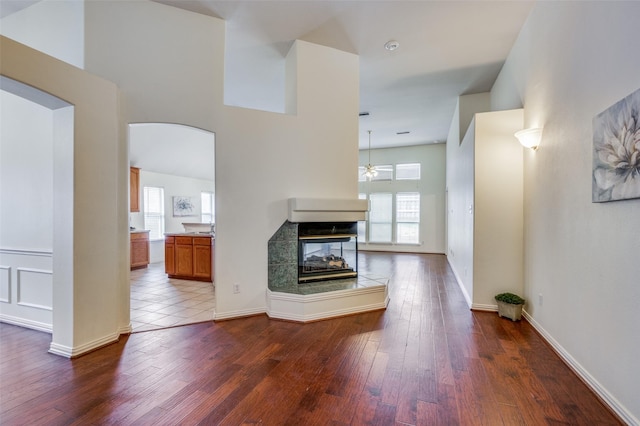 unfurnished living room with ceiling fan, a multi sided fireplace, arched walkways, and dark wood-style floors